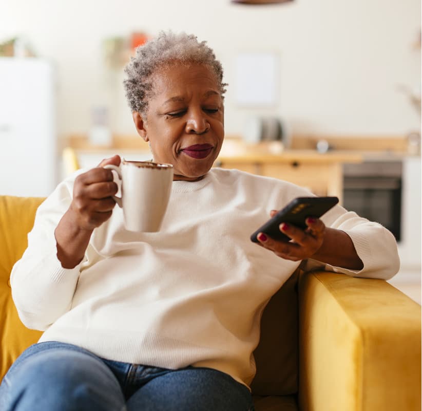 Older woman relaxing on her sofa with a mug, answering questions on her phone