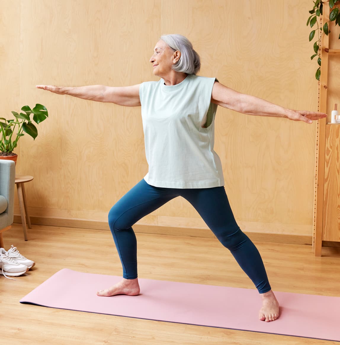 Older woman holding a standing yoga pose on an exercise mat